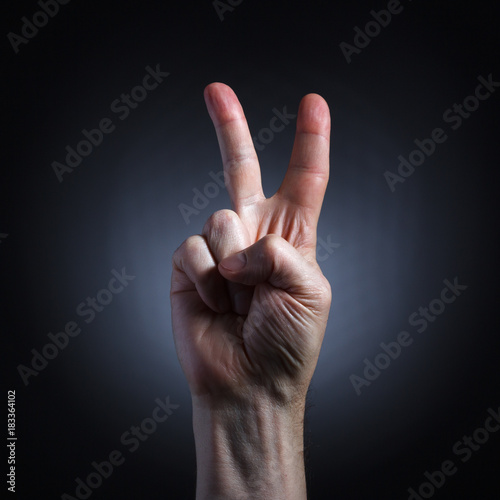 The human hand in a gesture of victory closeup on dark background. © papa