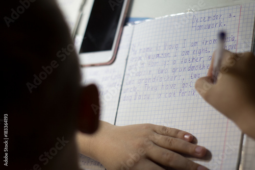 Close-up of boy hand with pencil writing english words by hand on traditional white notepad paper. photo