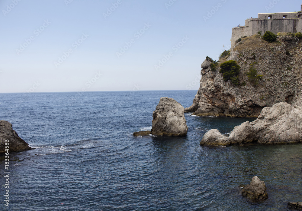 View of rocks and mediterranean sea at the bottom of Dubrovnik old town. It is a city in southern Croatia fronting the Adriatic Sea. View of rocks and mediterranean sea at the bottom of Dubrovnik old town. It is a city in southern Croatia fronting the Adriatic Sea.