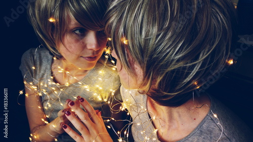 Fotografía Mujer joven rodeada de luces de navidad reflejándose en un espejo