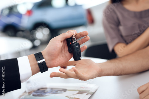 The seller in the car showroom gives the car keys to the buyer.