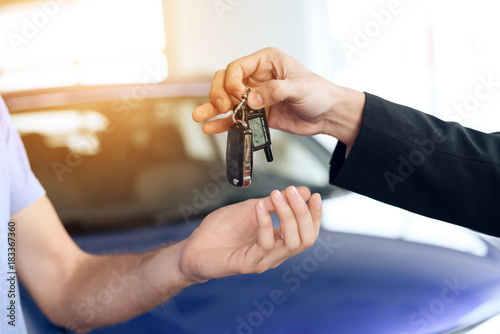 The seller in the car showroom gives the car keys to the buyer.