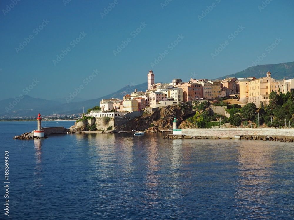 Corsica Bastia port view from sea on harbor with red and green lighthous church and old town blue sky background