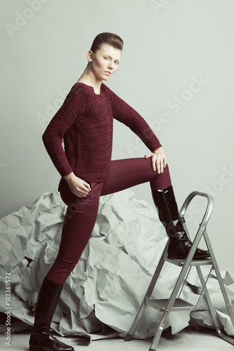 Art fashion, pret-a-porter concept. Full length portrait of androgynous model with short hair marching over gray background. Pale skin, natural make-up. Futurism style. Studio shot photo