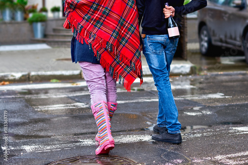 Young woman - girl with long hair in glasses, wearing rubber boots, with champagne and a glass, smiling happily, crossing the street turning.