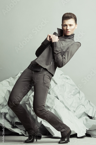 Strike a pose, haute couture concept. Full length portrait of androgynous model with short hair holding lapels, posing over gray background. Pale skin, natural make-up. Futurism style. Studio shot photo