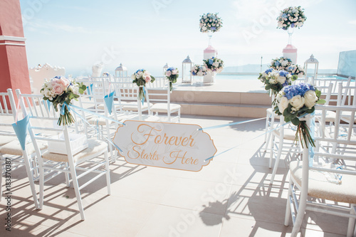 Fototapeta Naklejka Na Ścianę i Meble -  The location of the wedding ceremony on the island of Santorini with white chairs decorated with bouquets of flowers