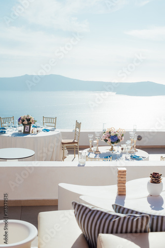 Fototapeta Naklejka Na Ścianę i Meble -  Vertical photography of place for a wedding dinner on the island of Santorini with white tables with decor and sea view