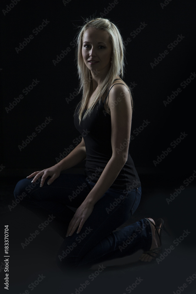 Beautiful blond woman in denim and black top kneeling in dark with selective lighting