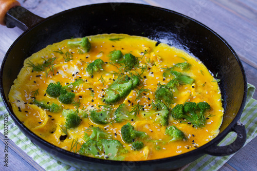 Omelette with broccoli and herbs, toasted with sesame seeds on frying pan, horizontal