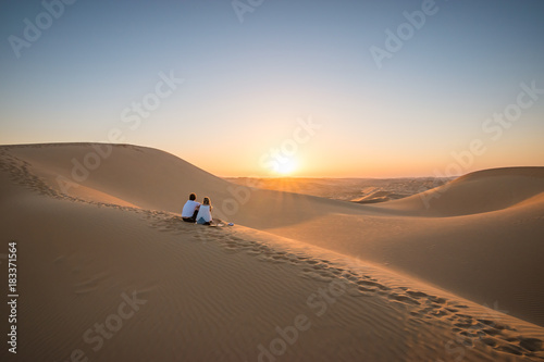 Desert landscape with young couple looking at sunset.