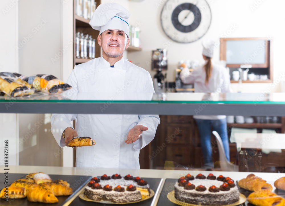Portrait of middle aged man baker with tasty cakes smiling in bakery