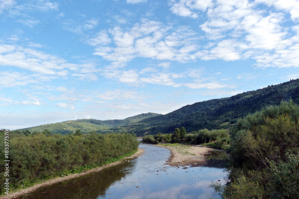 Panorama of the cloudy sky above the mountain forests and the river in the Ukrainian Carpathians.
