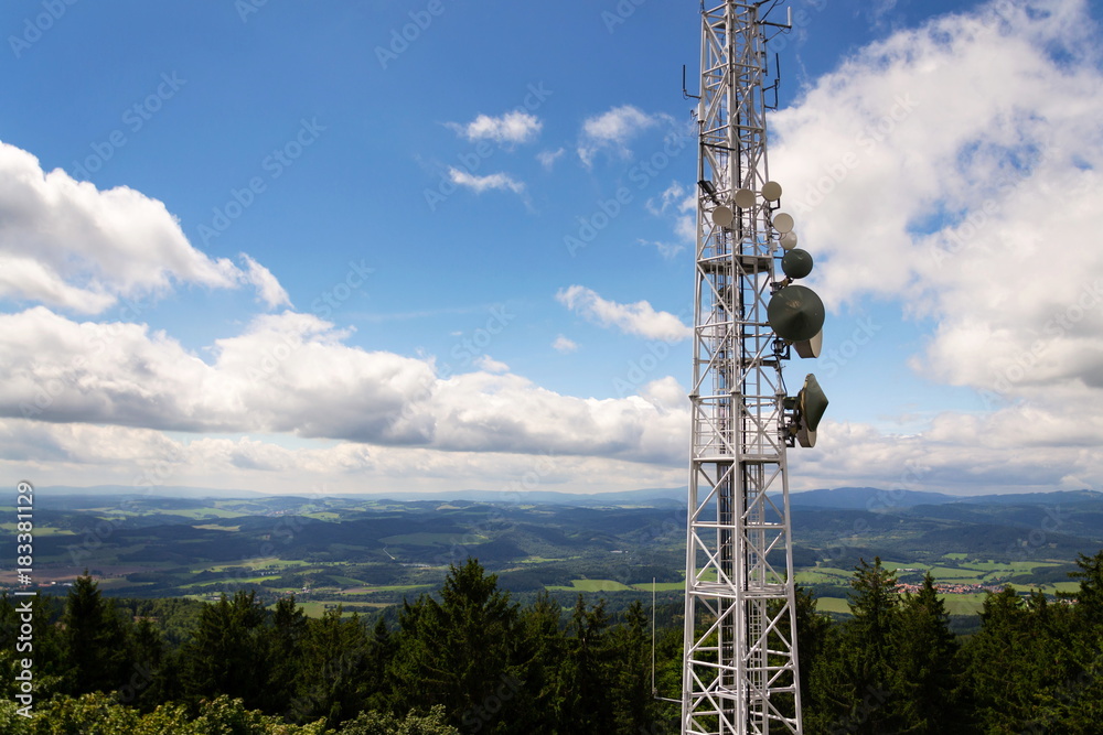Aerials and transmitters on telecommunication tower with mountains in background, cloudy blue sky, digital communication and encryption safety concept