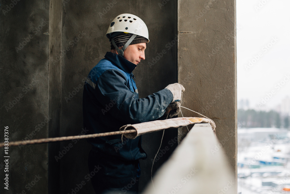 Construction worker in uniform and helmet preparing rope..Risky work at height Construction worker in uniform and helmet preparing rope..Risky work at height