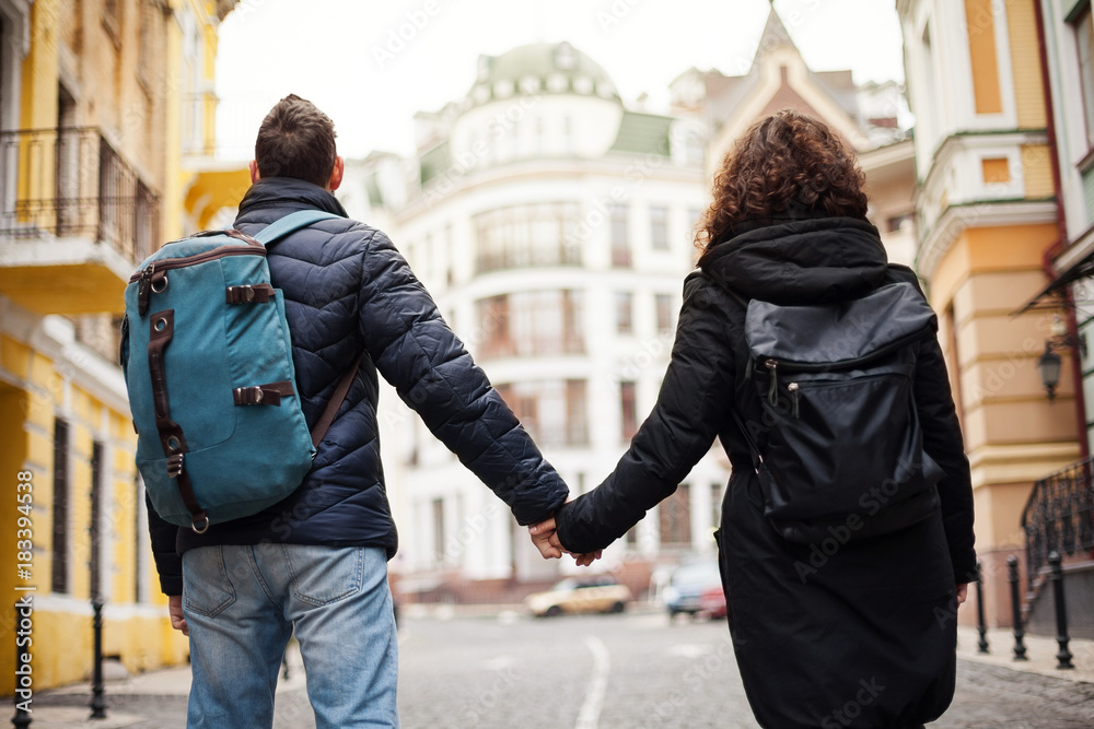Back view of the young couple with backpacks, the whole world is ahead. A man and a girl are holding each other's hands.