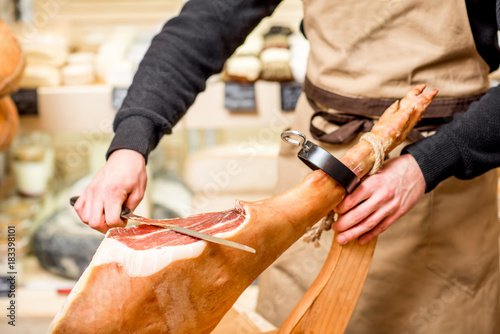 Cutting with long knife prosciutto leg in the food store photo