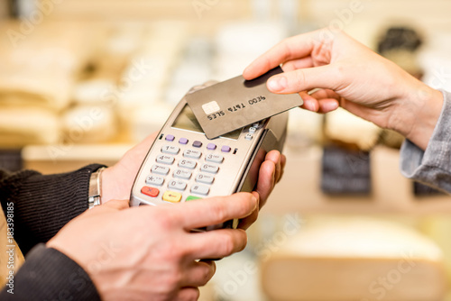 Woman paying with card contactless in the food store. Close-up view on the terminale and card photo