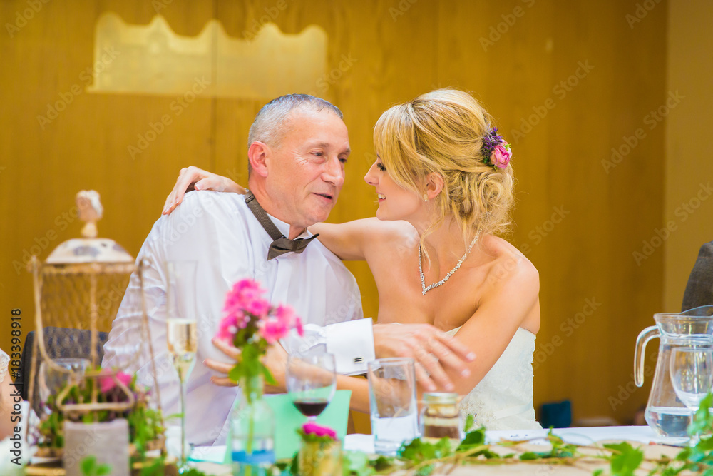 The young happy beautiful bride sitting by the table with her happy father in embrace in restaurant The young happy beautiful bride sitting by the table with her happy father in embrace in restaurant
