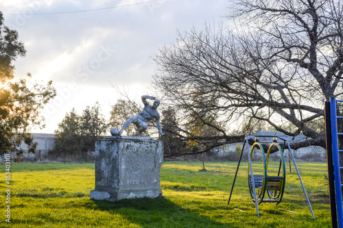 Monument to the football player at the stadium. Children playground. Swings and a slide to slide photo