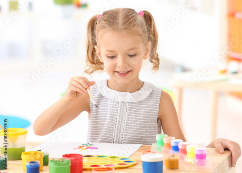 Cute girl painting picture at table indoors