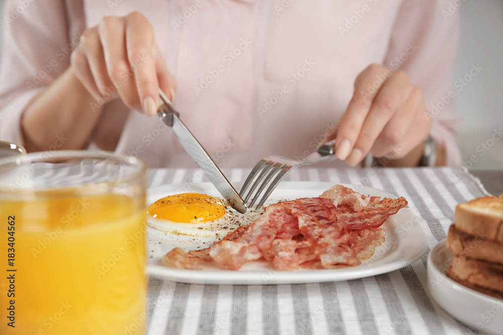 Young woman eating fried egg and bacon at table
