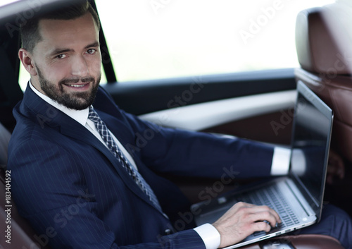 Confident businessman with laptop sitting in auto.