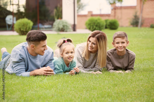 Happy family lying on green grass in courtyard near their house