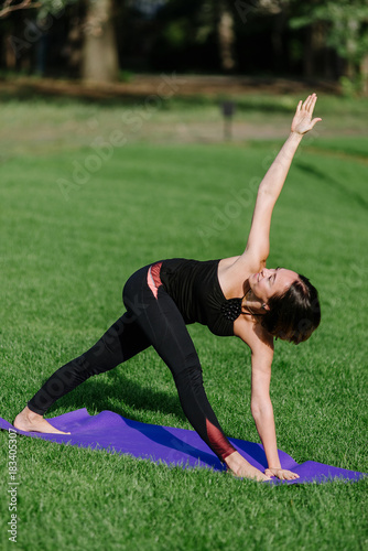 the girl is engaged in yoga in the park on the grass.