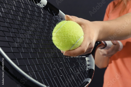 Woman with tennis racket and ball on dark grey background