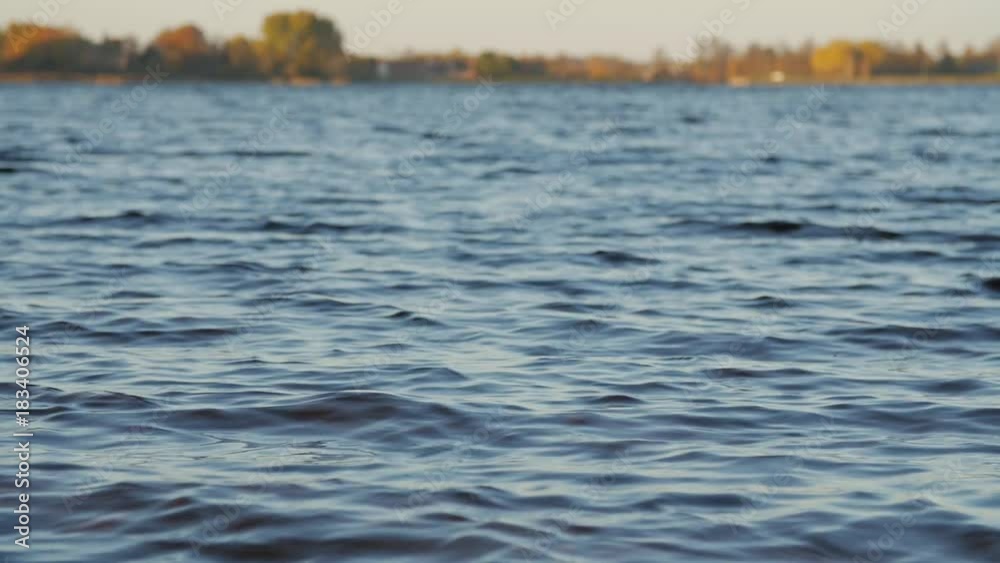 View of the lake and waves from the low shore.Calm water background. Telephoto lens shot with shallow depth of field. Low angle view, slow motion. View of the lake and waves from the low shore.Calm water background. Telephoto lens shot with shallow depth of field. Low angle view, slow motion.