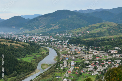 A beautiful view of the village of Mezhgorye, Carpathian region. A lot of residential buildings surrounded by high forest mountains and long river photo