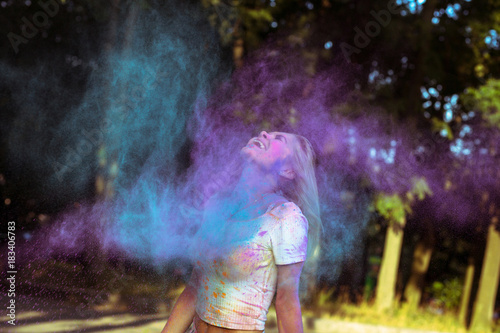 Expressive blonde woman with fluttering hair playing with Holi powder exploding around her