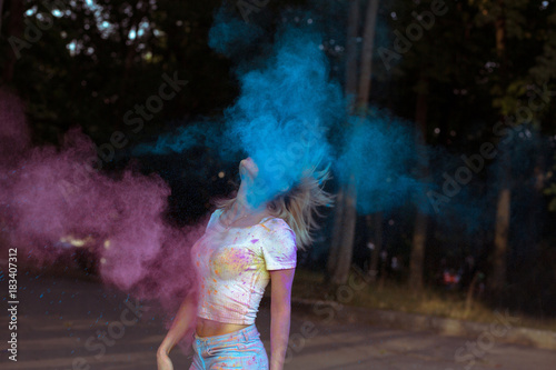 Pretty young woman with hair in motion playing with Holi powder exploding around her