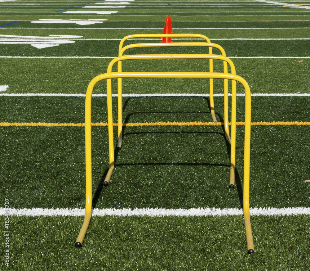 Yellow mini hurdles and orange cones on green turf field Yellow mini hurdles and orange cones on green turf field