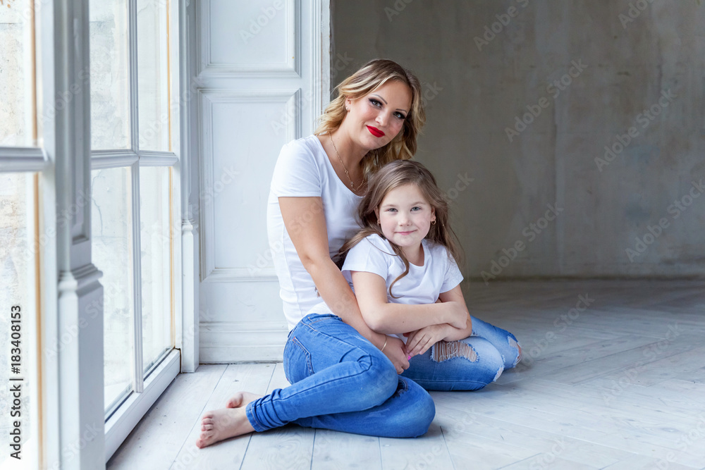 Young mother holding her child. Woman and little girl relax in a white bedroom near the window. Happy family at home. Young mother playing with her daughter Young mother holding her child. Woman and little girl relax in a white bedroom near the window. Happy family at home. Young mother playing with her daughter