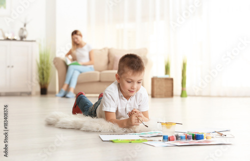 Cute boy painting picture on sheet of paper, indoors