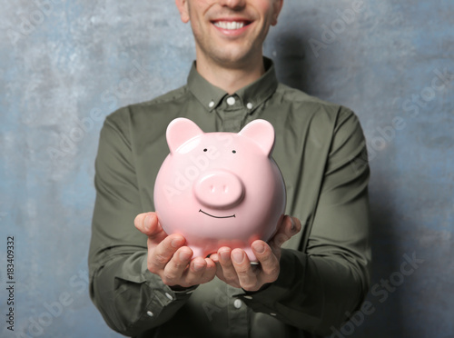 Young man with piggy bank on grunge background