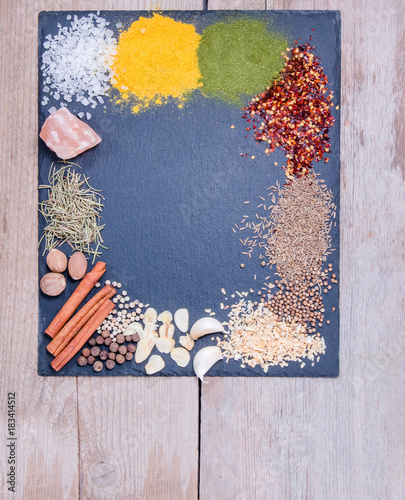 Natural spices and herbs scattered on slate tray on an old rustic table. Natural and bio ingredients for cooking. Organic products. Copy space for your text.