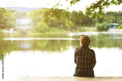 Woman from back sitting alone on dock and looking for a lake view