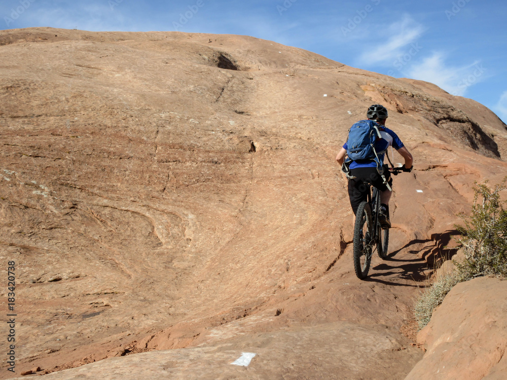 Fototapeta premium Mountain biker climbing a sandstone hill at Slickrock mountain biking trail in Moab, Utah