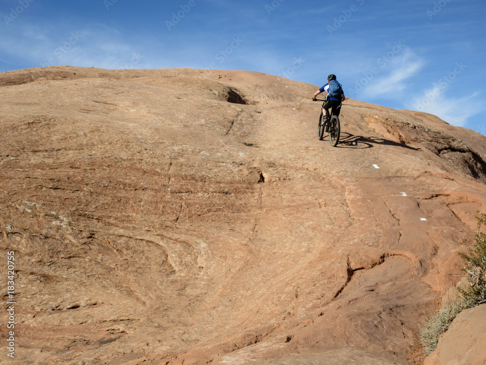 Fototapeta premium Mountain biker climbing a sandstone hill at Slickrock mountain biking trail in Moab, Utah