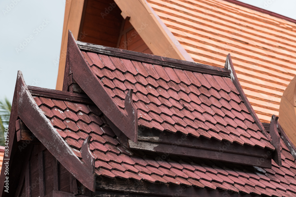 detail of traditional thai house roof style and eave board with wooden shingle and clay tiles