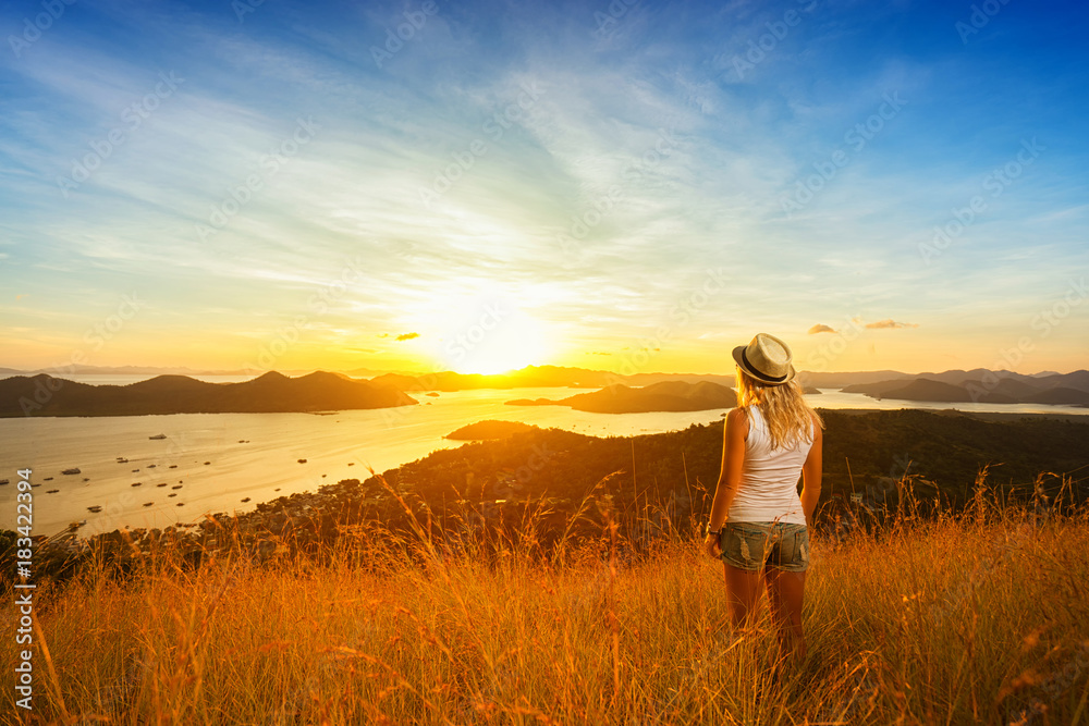 Woman enjoying sunset from mountain top. Islands and sky on background. Back view.