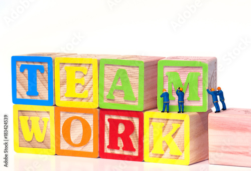 Teamwork - Miniature construction worker figurines posed as if building the word Teamwork with toy blocks.