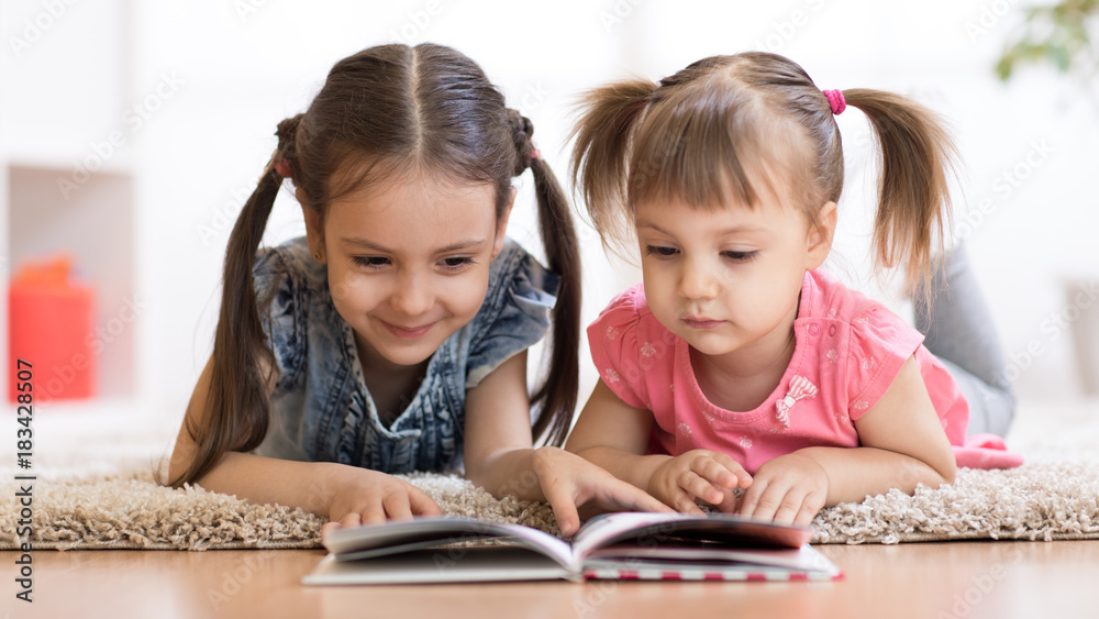 Child girl reading book with little sister at home Child girl reading book with little sister at home