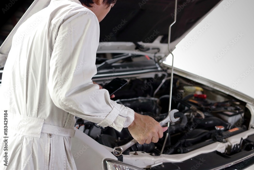Rear view of automotive mechanic in white uniform with wrench diagnosing engine under hood at the repair garage. Car insurance concept. Rear view of automotive mechanic in white uniform with wrench diagnosing engine under hood at the repair garage. Car insurance concept.