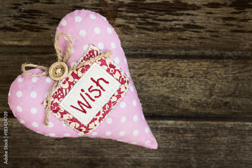 Pink dotted handmade fabric heart with word WISH on wooden background, top view