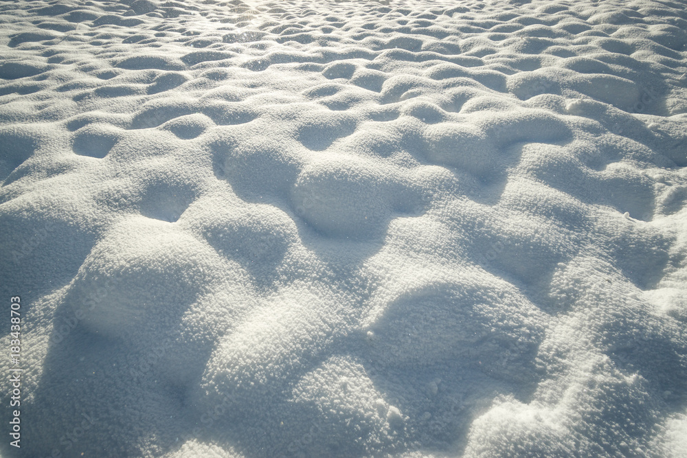 Obraz premium Fresh hilly snow surface background and drifting snowflakes. Bumpy snow covering winter landscape.
