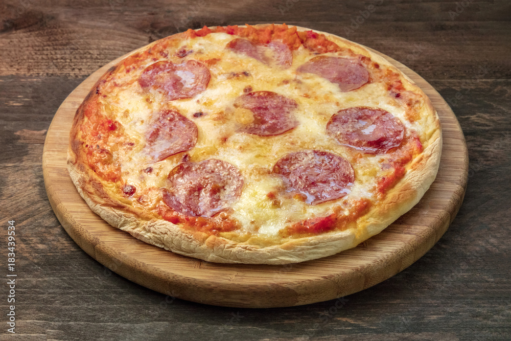 Pepperoni pizza on pizza stone and rustic texture, closeup photo